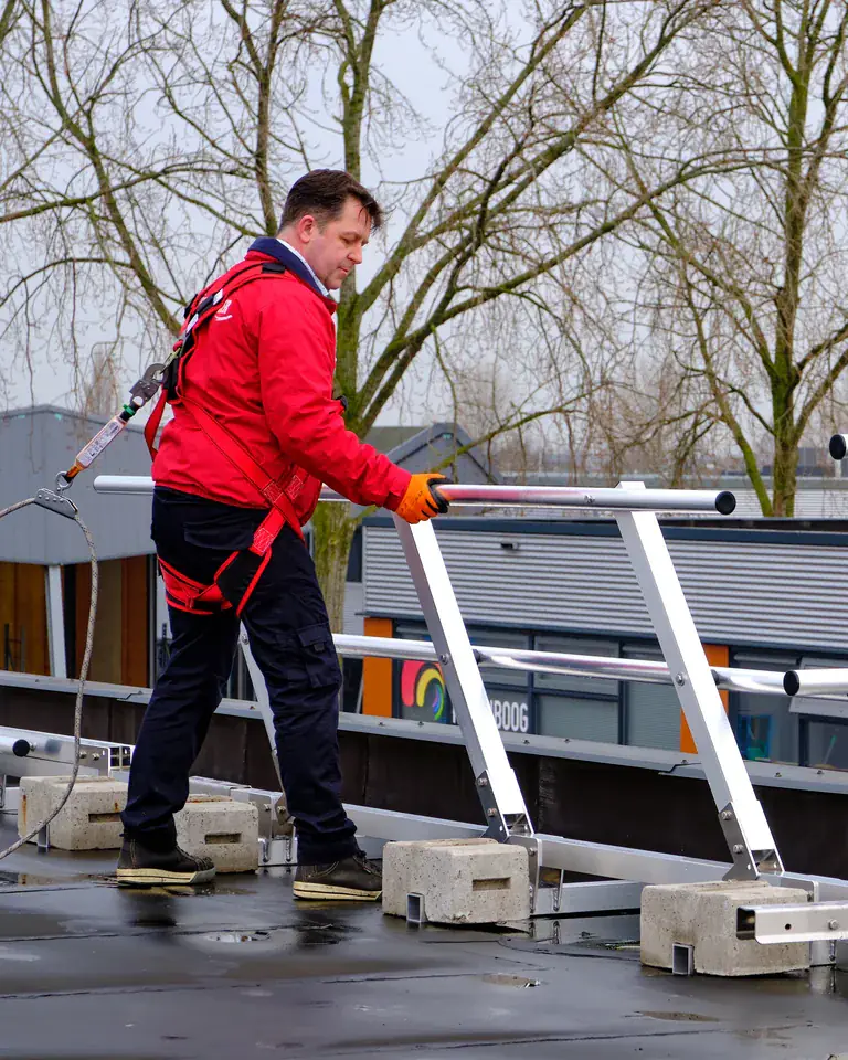 Facilitytechnieker in valbeveiliging installeert een dakreling op een plat dak
