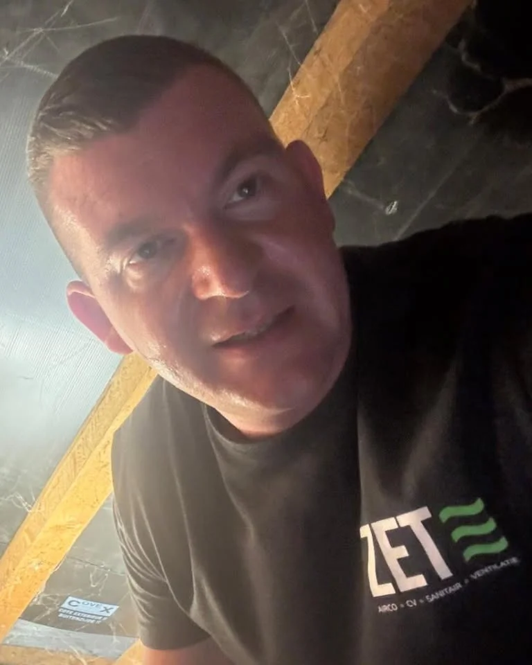 Zet-installateur in kruipruimte kijkt recht in de camera, ZET-logo op zijn shirt